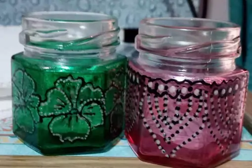 A pair of upcycled candle glass jars, hand-painted in complimentary colours with patterns and floral designs.